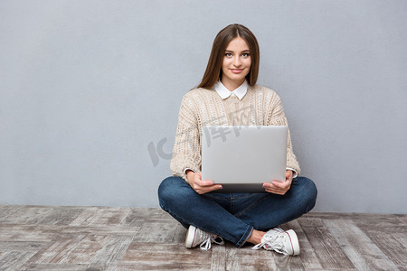 使用笔记本电脑坐在木地板上的年轻自信的女人