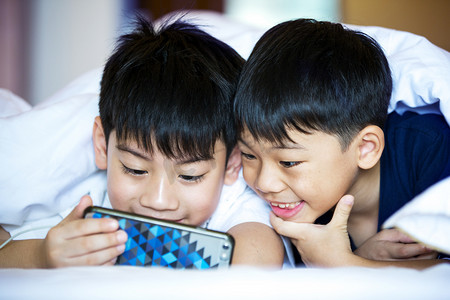 亚洲学龄前的男孩一起玩智能手机 