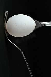 铁质叉子摄影照片_黑色背景上有一个鸡蛋和两个叉子