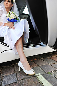 美丽的新娘坐在车里。穿白鞋的腿