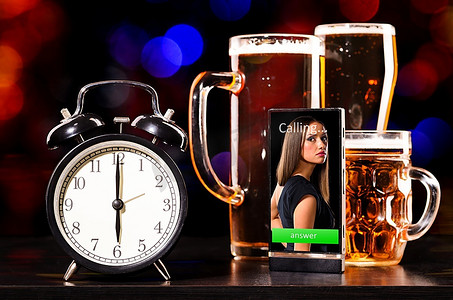 喝啤酒摄影照片_喝啤酒的时间到了。一杯带闹钟和手机的新鲜啤酒