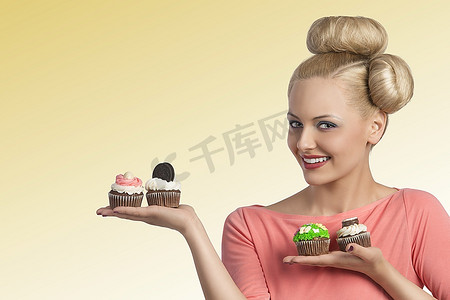 年轻漂亮的金发女郎，发型别出心裁，妆容五颜六色，展示了各种各样的糖果和纸杯蛋糕
