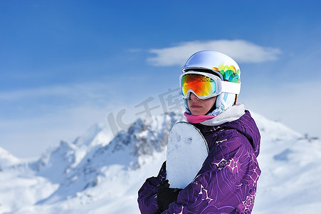 一名女子手持滑雪板，背景是山脉。没有品牌名称或版权对象。