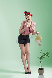 园艺标语摄影照片_性感的金发女园丁的肖像，穿着性感的标语，拿着水壶，微笑着
