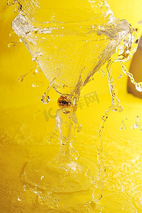 黄色液体摄影照片_冷透明的水在鸡尾酒杯和飞溅的黄色