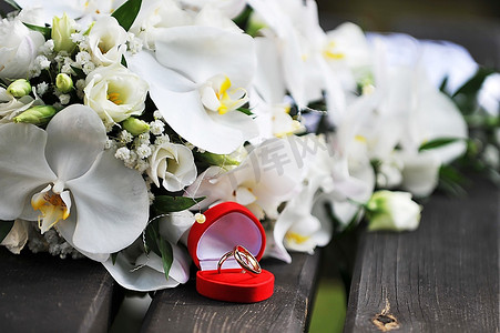 花束的白色兰花和婚礼金戒指在木长凳上