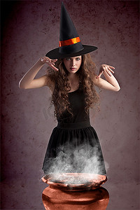 漂亮的大锅摄影照片_年轻漂亮的女孩在万圣节前夕戴着一顶巨大的黑色女巫帽子在女巫后面施咒&敏锐；S大锅