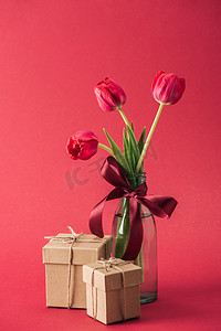 花束红色郁金香与红色缎子弓和礼品盒在红色背景