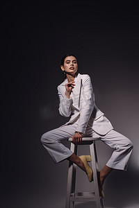 建模头摄影照片_时尚的年轻女子穿着白色西装坐在椅子上的黑暗背景