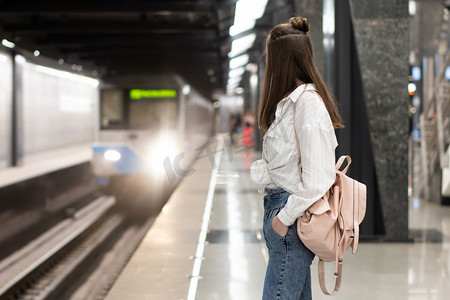 阿里山的姑娘摄影照片_穿着牛仔裤和衬衫背着背包的年轻的欧洲姑娘在地铁站等火车。 运动的背景模糊了传达一种生机勃勃的气氛. 这是一个快照的主意.