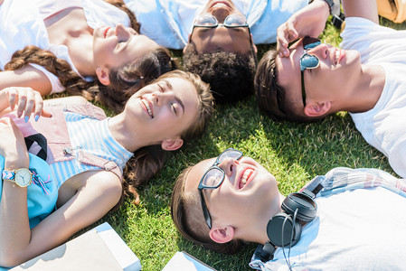 在绿色草地上躺在一起的快乐多民族青少年朋友的高角度视图