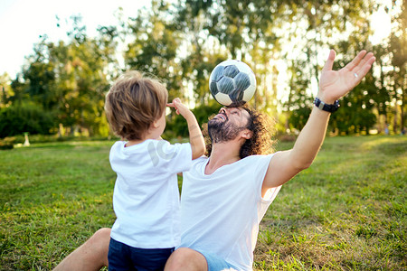 抱抱摄影照片_父亲儿子在公园的草地上玩球.
