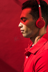 帅气的混血男子的侧视图在耳机与眼睛闭上红色与复制空间