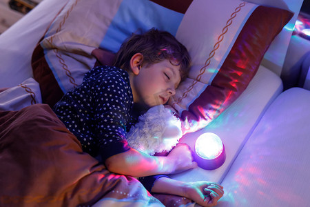 宝贝晚安摄影照片_用彩色灯在床上睡觉的小学龄前孩子男孩.