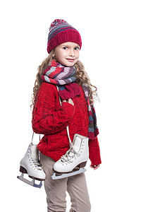 可爱微笑的小女孩与卷曲的发型，穿着溜冰鞋在白色背景上孤立针织的毛衣、 围巾、 帽子和手套。冬天的衣服和运动概念.