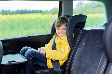 可爱可爱的学龄前孩子男孩坐在车里在黄雨外套.