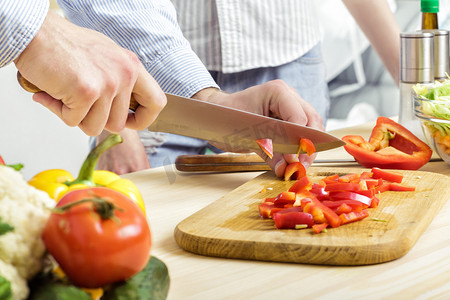 食品商务摄影照片_男人的手切碎的红辣椒在船上。切菜在厨房里的夫妇