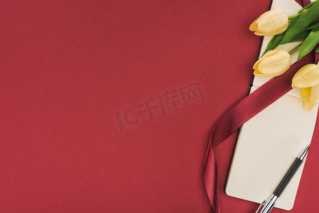 国际模板摄影照片_带丝带的郁金香和用红色隔开的空笔记本的顶部视图