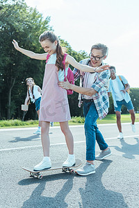 快乐的少年男孩教女孩在公园骑滑板