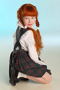 红色商务图摄影照片_穿着校服的漂亮小红头发女孩蹲着。开朗迷人的孩子与苗条的身体和苗条裸露的腿。这个年轻的女学生8岁了。.