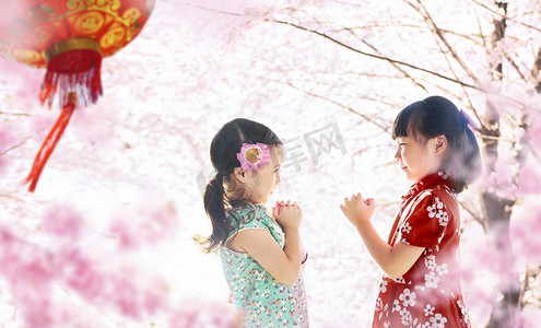新年衣服摄影照片_两个女孩站在樱花园对面, 在模糊的背景, 中国的新年季节
