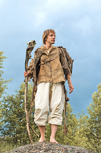 神话故事国潮插画摄影照片_穿着粗麻布衬衫的乡下人站在一根木棍上的石头上。