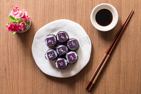 背景米白色摄影照片_寿司-紫甘薯在寿司米白色的陶瓷板。紫心甘薯的好处是高 β-胡萝卜素和用于烹饪的碳水化合物。顶视图