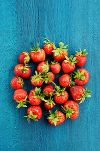 水果新鲜不新鲜摄影照片_新鲜不完美草莓在青绿色背景上的圆形状 