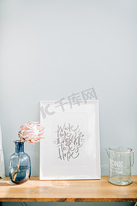 粉商务摄影照片_相框与书法报价那里有光明有希望, 普罗蒂亚花在花瓶前面的粉彩蓝墙.
