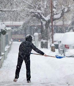 冬季下雪房子摄影照片_在大雪后铲雪从人行道上的女人