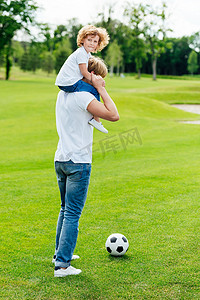 綠草地摄影照片_父亲和儿子在公园中踢足球