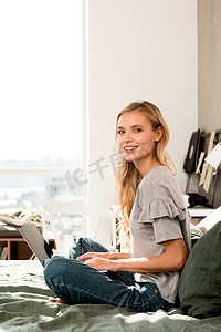 漂亮的微笑的女人, 笔记本电脑坐在家里的床上