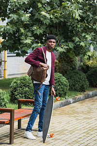 英俊的年轻学生与背包和滑板站在街上