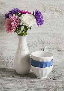 秋花紫苑在一个白色的花瓶和光的木制表面陶瓷碗