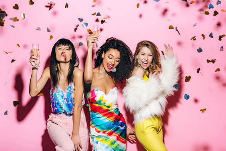 国际幸福日摄影照片_兴奋的多文化女孩，一边喝着粉红色的香槟酒，一边吃着五彩纸屑