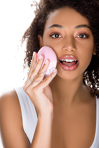 护肤摄影照片_令人惊讶的非洲裔美国女孩，带着牙套，用硅胶清洁面部刷，用白色隔开