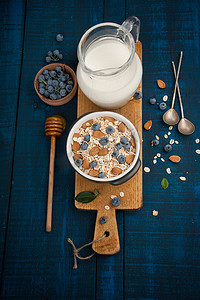 酸奶燕麦摄影照片_蓝底白字黑木制健康的早餐: 燕麦粥、 牛奶、 蓝莓、 蜂蜜和杏仁。乡村风格.
