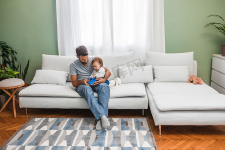 帅气的爸爸摄影照片_英俊的白种人坐在家里和他的小儿子玩.