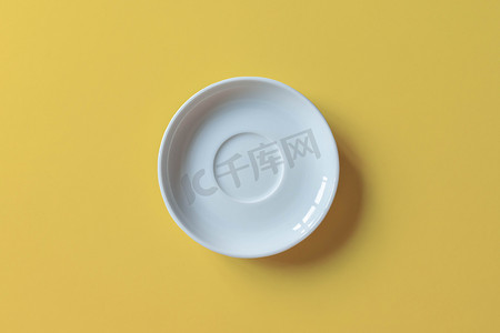白色的蛋糕盘放在黄色的背景上.在黄色背景上隔绝的空陶瓷圆盘.平躺在床上顶部视图.