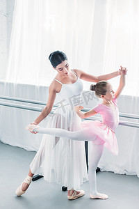 优雅老师摄影照片_高角度看可爱的孩子在粉红色的芭蕾舞短裙芭蕾学校与年轻教师的芭蕾练习  