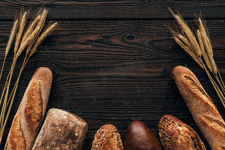 面包造型摄影照片_面包和小麦在木质表面排列游荡的顶部视图