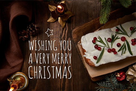 圣诞摄影照片_上图是传统圣诞蛋糕，在松树旁的覆盆子和木制桌子上的蜡烛装饰着越橘，祝你圣诞快乐