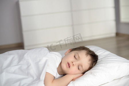 衾摄影照片_男孩睡在床上，快乐睡前在白色卧室