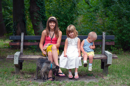 t恤多色摄影照片_少女跟她年轻得多的哥哥和姐姐在公园里的坐在一起