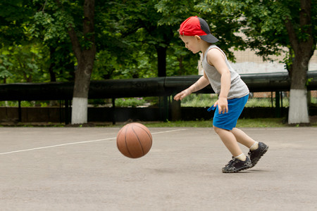 树木的孩子摄影照片_在法庭上弹跳篮球的小男孩
