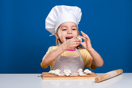 The little girl is cooking and preparing food on blue background