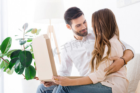 微笑的夫妇与比萨在纸箱子坐在沙发在家