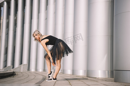 年轻芭蕾舞女演员的侧视图看着相机在城市街道上的黑色裙子