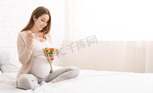 快乐的怀孕少女坐在沙发上吃着水果沙拉