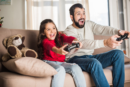 孩子电子游戏摄影照片_兴奋的父亲和女儿在家里玩电子游戏